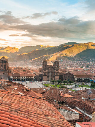 Panoramic view of the historic city of Cusco in Peru, featuring terracotta tiled rooftops and colonial buildings surrounded by majestic mountains.