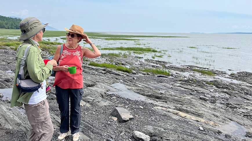Two women hiking on the rocky shoreline of Île d'Orléans in Québec, overlooking the water.