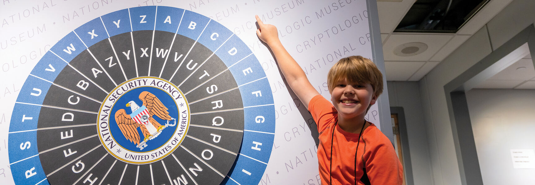 A smiling child points at a large NSA cryptologic wheel display at the National Cryptologic Museum in Washington, D.C.