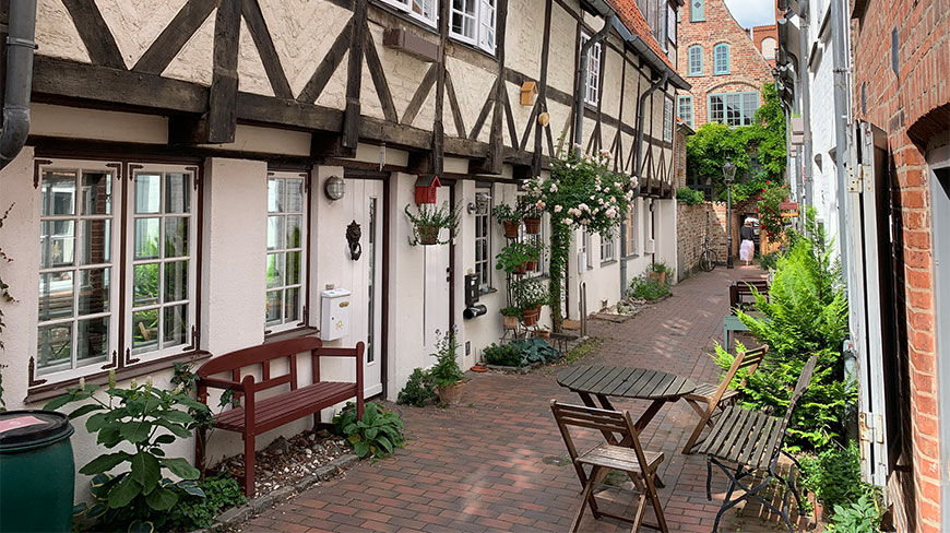 A narrow brick alley in the historic Schnoor Quarter of Bremen, Germany, is lined with charming half-timbered houses and potted plants.