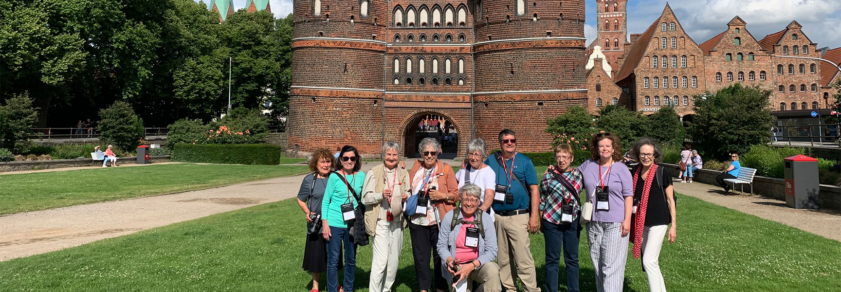 A group of travelers smiling for a photo in front of the historic Holstentor city gate in Lübeck, Germany.