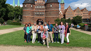 A group of travelers stands on the lawn in front of the historic Holstentor city gate in Lübeck, Germany.