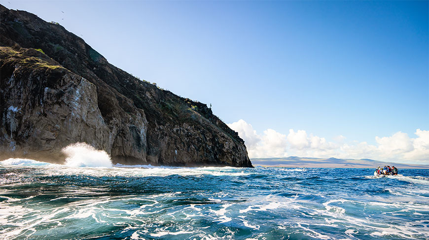 A panga ride navigates blue waters near the dramatic rocky cliffs of Cerro Brujo and Isla Lobos in the Galapagos Islands.