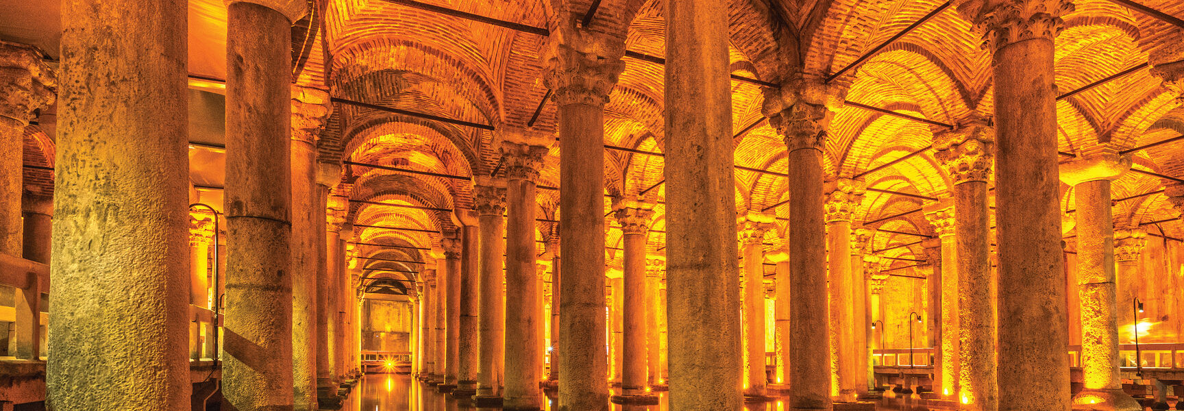 The illuminated stone columns and vaulted brick ceilings of the Basilica Cistern in Istanbul reflecting in the shallow water below.