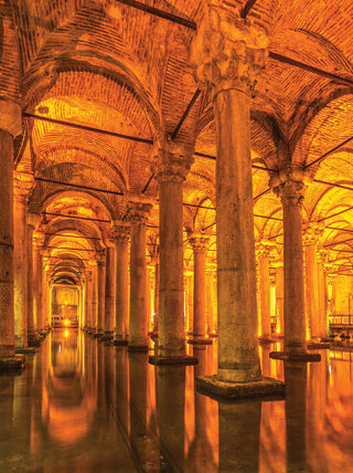 The illuminated stone columns and vaulted brick ceilings of the Basilica Cistern in Istanbul reflecting in the shallow water below.