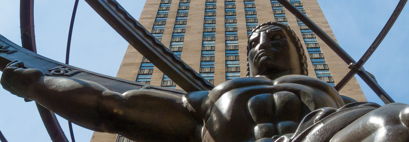 A low-angle shot of the bronze Atlas statue in front of a skyscraper at Rockefeller Center under a clear blue sky.