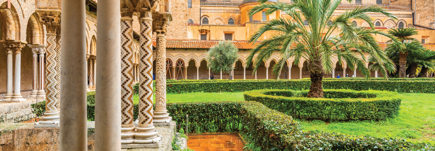 Historic courtyard garden in Sicily, Italy, featuring ornate stone columns and lush palm trees, showcasing the region's rich architectural and cultural history.