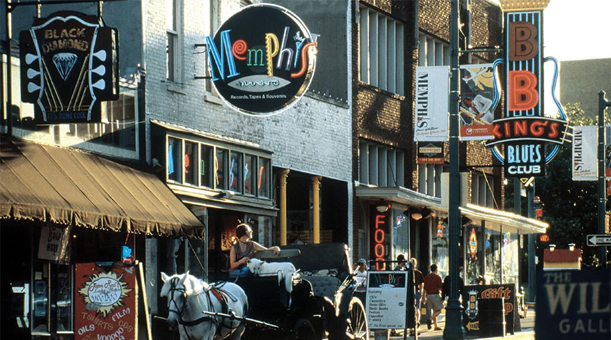 A vibrant Memphis street scene with neon signs for blues clubs, shops, and a horse-drawn carriage in the foreground.