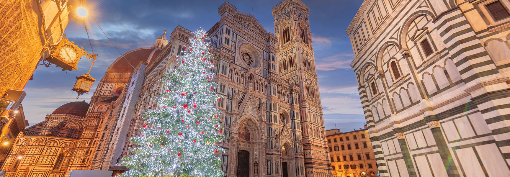An illuminated Christmas tree stands in front of the historic Florence Cathedral and bell tower during the holiday season in Florence, Italy.