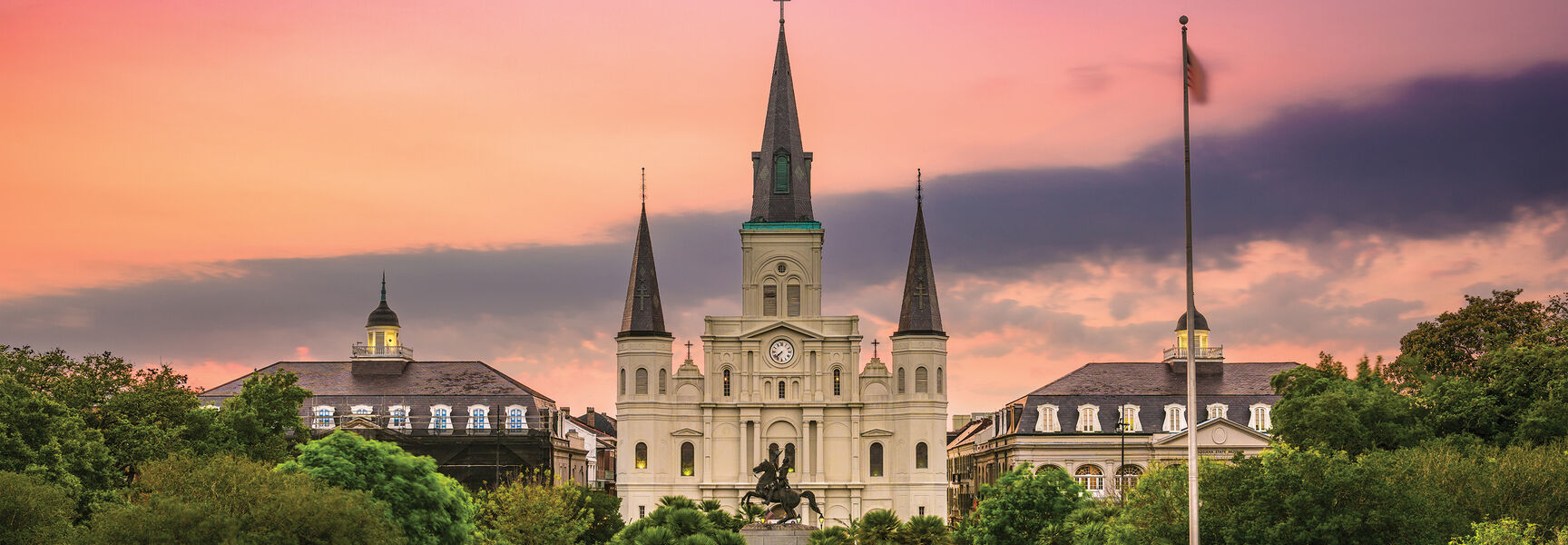 Horse-drawn carriages line the street before St. Louis Cathedral in a historic district of New Orleans, Louisiana, under a vibrant sunset sky.