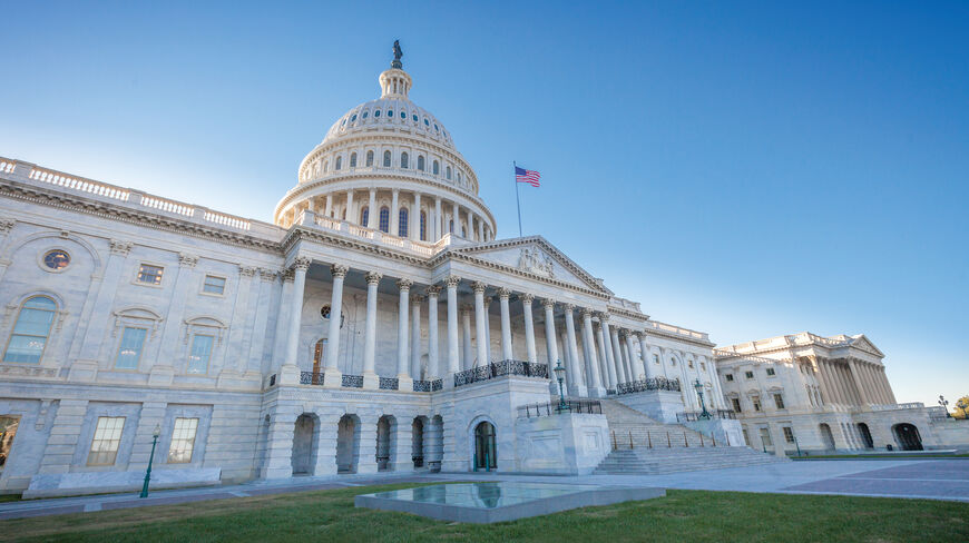 A low-angle, historic view of the United States Capitol building in Washington, D.C., featuring its white dome and marble columns under a clear sky.