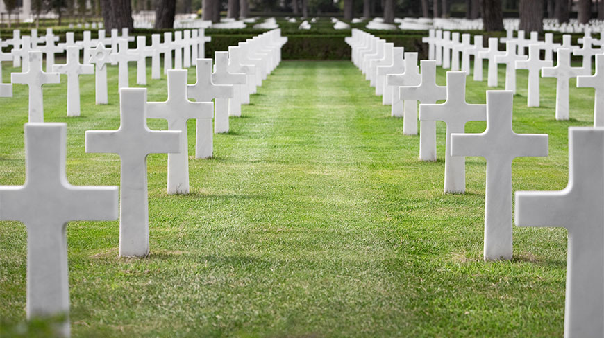 Symmetrical rows of white marble crosses and Stars of David stand in the green grass at the Sicily-Rome American Cemetery.