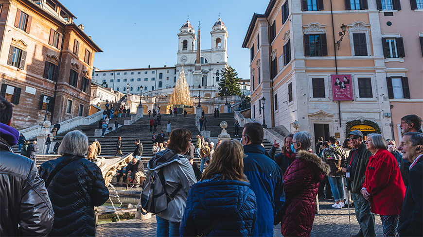 A large crowd of tourists gathers at the base of the Spanish Steps in Rome, Italy, leading up to the Trinità dei Monti church.