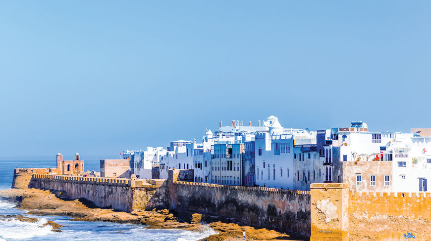 White buildings and historic stone sea walls of Essaouira, Morocco, overlook the crashing waves of the Atlantic Ocean.