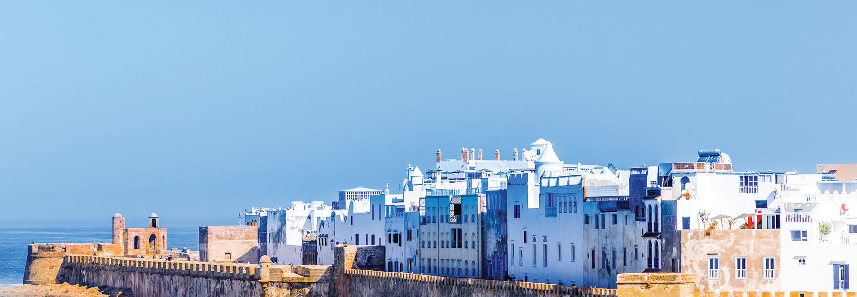 White buildings and historic stone sea walls of Essaouira, Morocco, overlook the crashing waves of the Atlantic Ocean.