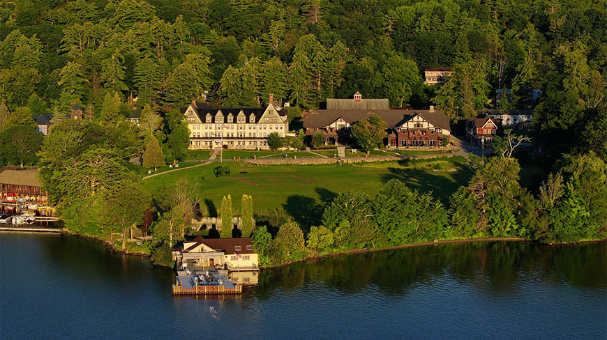 Aerial view of The Inn and Boyd Center in New York, overlooking a lush green lawn and the calm waters of a lake.