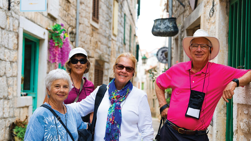 Four smiling senior travelers pose in a narrow, sunlit stone alleyway during a Voyage Through History tour of the Adriatic.