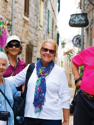 Four smiling senior travelers pose in a narrow, sunlit stone alleyway during a Voyage Through History tour of the Adriatic.