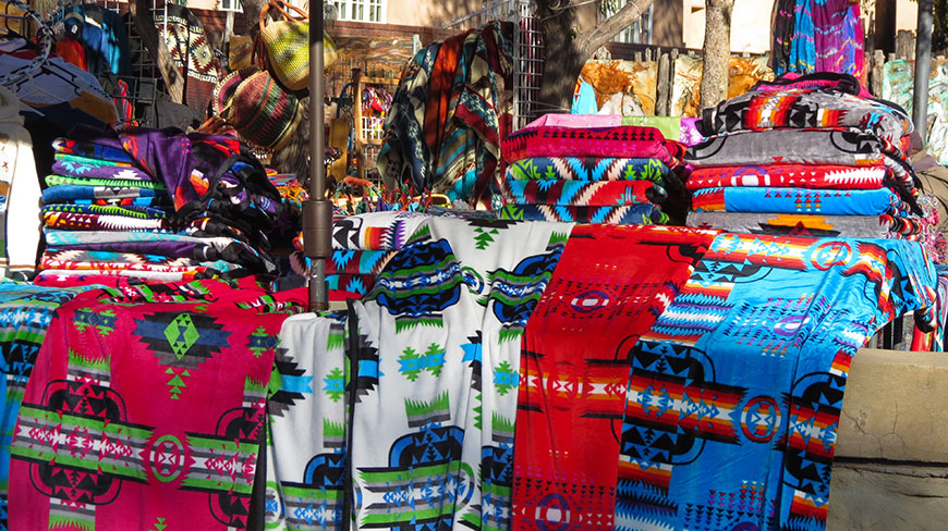 Vibrantly colored Southwestern-patterned blankets are displayed for sale at an outdoor market stall.