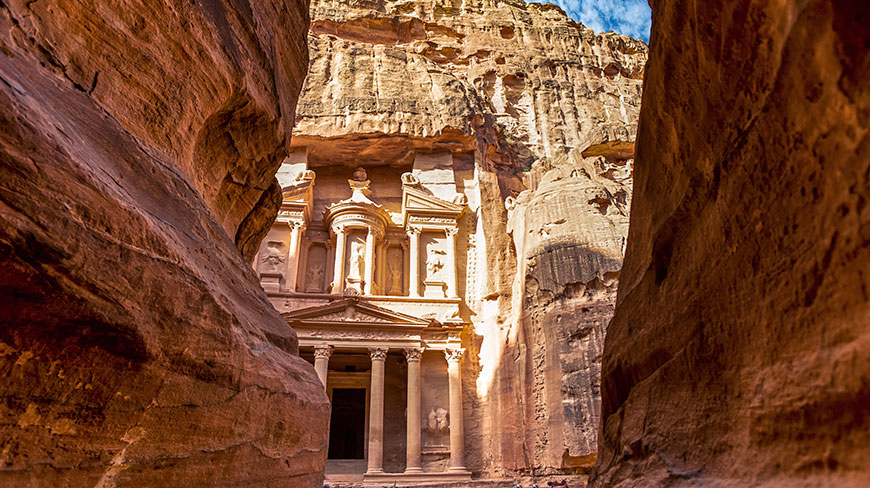The Treasury building at Petra is seen through a narrow opening in a red rock canyon.
