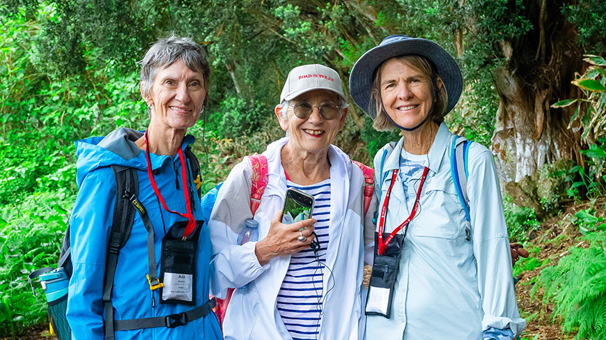 Three women smile together while on a group hike on a lush, green forest trail in Costa Rica.