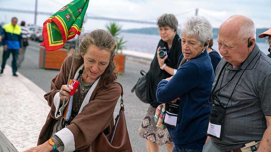 A tour guide holding a small Portuguese flag points something out to a group of older travelers on a guided tour.
