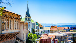 Colorful buildings built on a sunny hillside in Valparaiso, Chile, with a prominent church steeple rising among them.