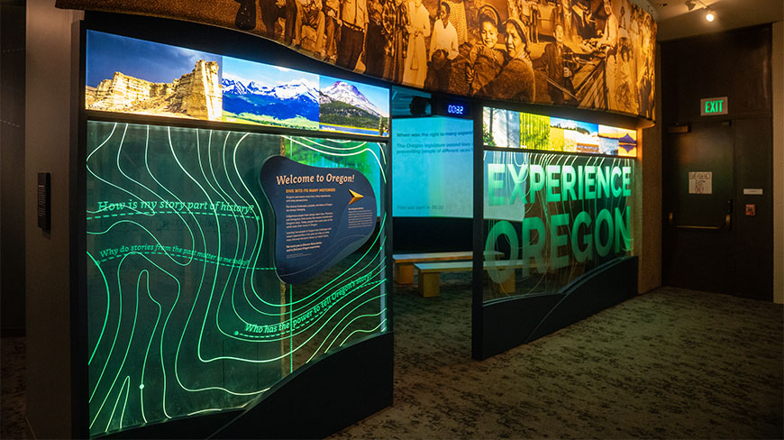 An exhibit at the Oregon Historical Society in Portland, featuring illuminated topographic lines and a large sign that reads "Experience Oregon."