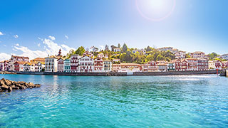 Panoramic view of colorful traditional Basque houses lining the harbor of Saint-Jean-de-Luz under a bright blue sky.