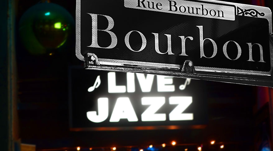 A close-up of a Bourbon Street sign in New Orleans with a glowing Live Jazz sign in the background.