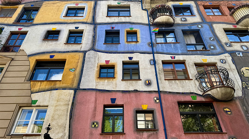 Vibrant and irregularly designed facade of the Hundertwasser House in Vienna, featuring colorful walls, uneven windows, and rounded balconies.