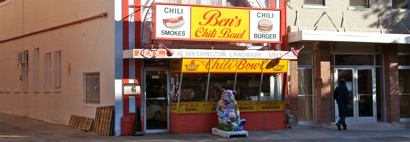 The exterior of Ben's Chili Bowl in Washington, D.C., a landmark restaurant with a bright yellow and red sign, on a sunny day.