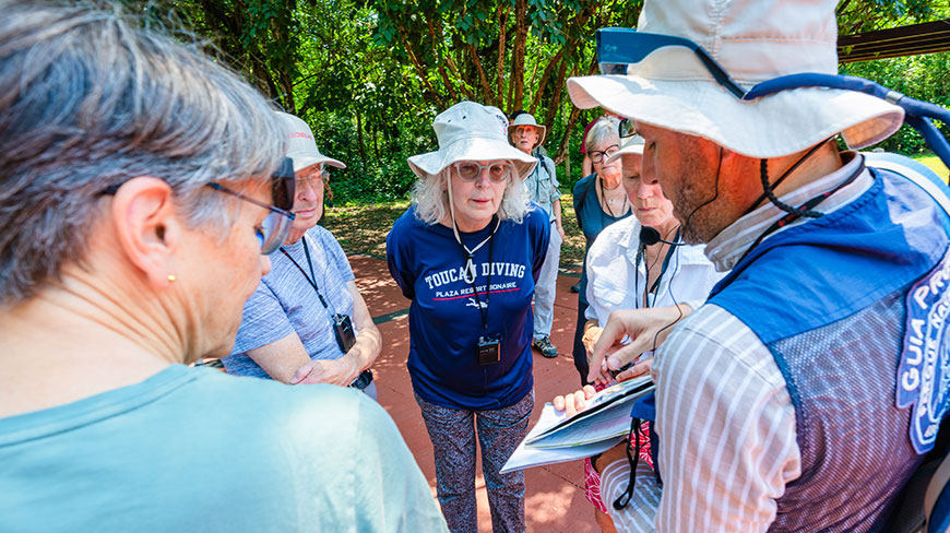 A tour guide points to a map while speaking to a group of visitors outdoors at Iguazu Falls National Park.