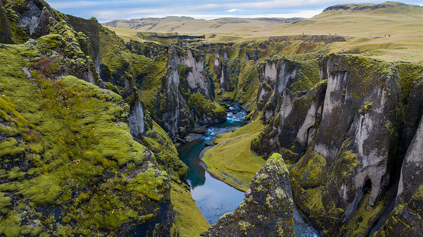 Deep Kirkjubæjarklaustur canyon featuring dramatic moss-covered cliffs and a winding blue river flowing through the Icelandic landscape.