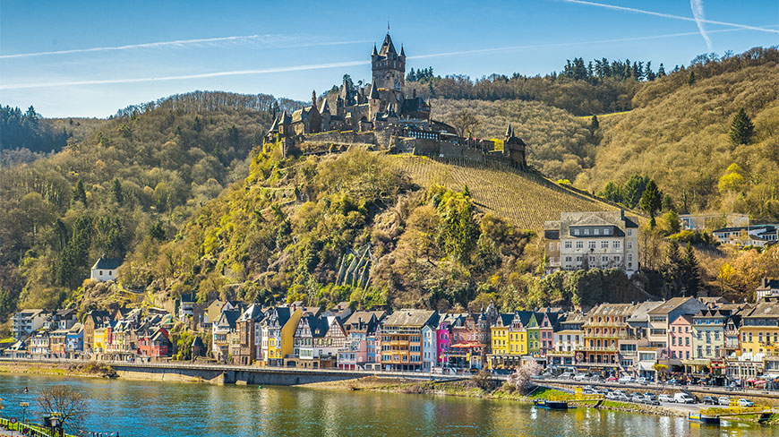 Reichsburg Castle sits atop a scenic hill overlooking colorful buildings along the Moselle River in Cochem, Germany.
