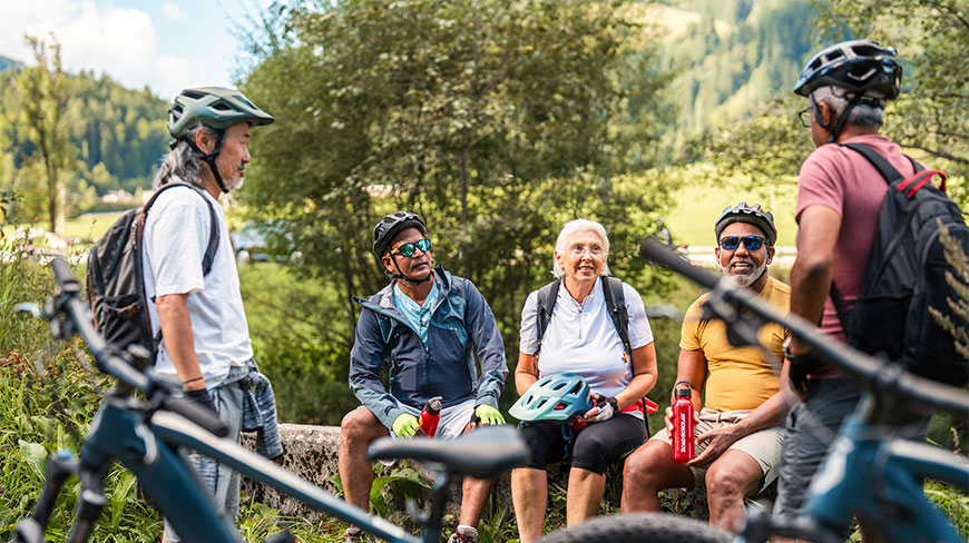 A group of diverse older adults biking take a break together in a scenic, mountainous landscape.
