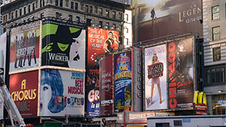 Colorful Broadway musical billboards including Wicked and Chicago line the streets of Times Square in New York City.