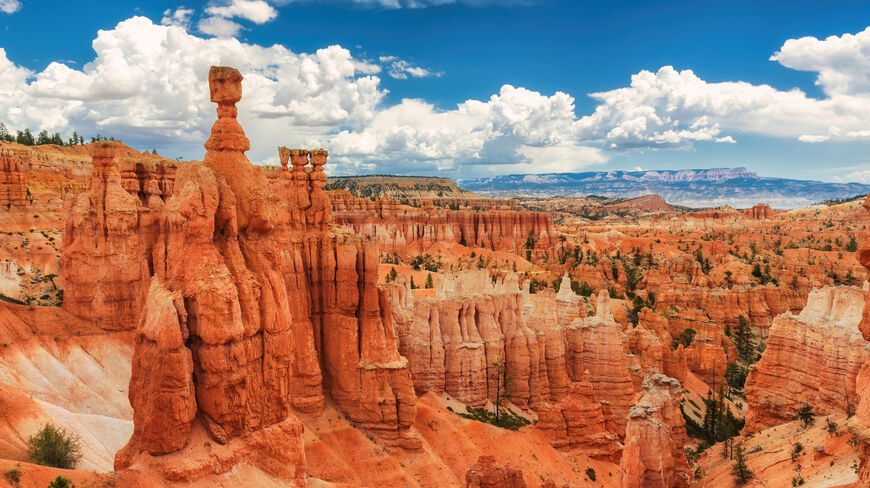 Vibrant orange hoodoos and rock spires fill the landscape of Bryce Canyon National Park in Utah under a sunny, cloud-filled sky.
