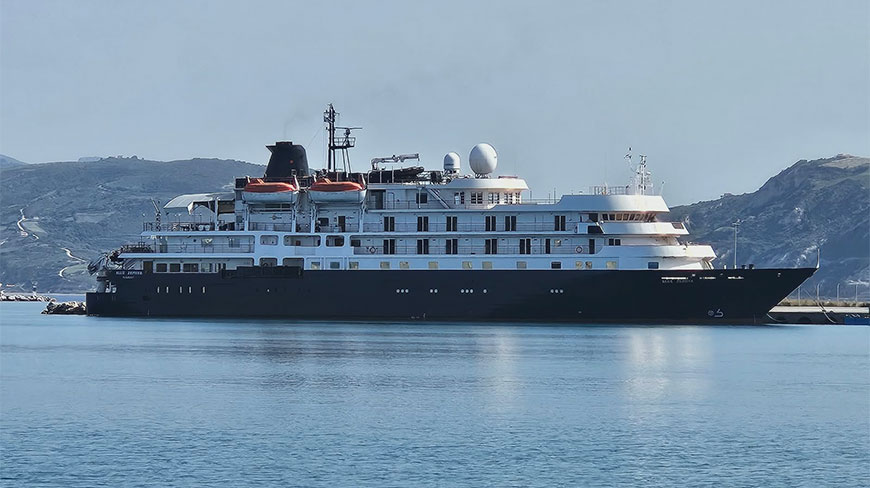 The Blue Zephyr cruise ship docked in a harbor with coastal mountains in the background.