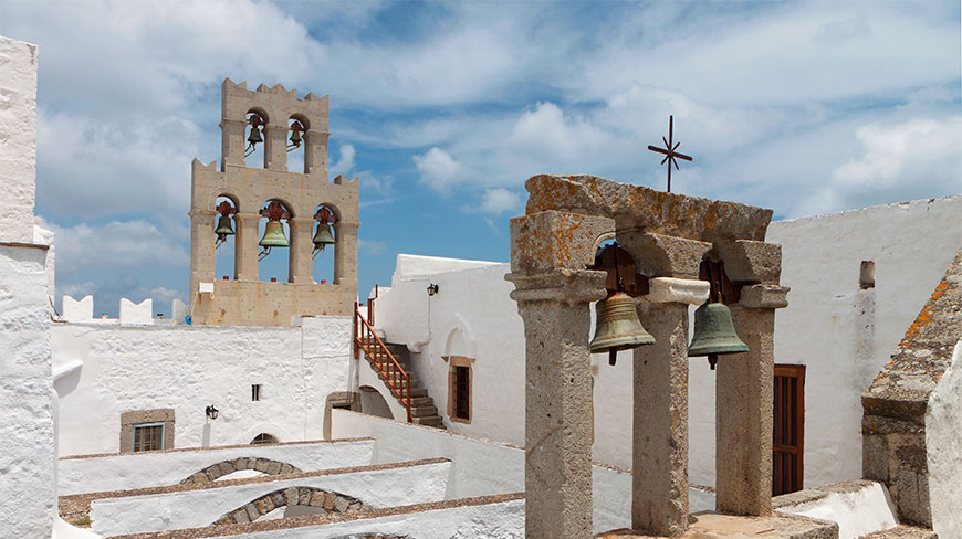 Stone bell towers with bronze bells rise above the whitewashed walls of St. John Monastery on Patmos Island, Greece.