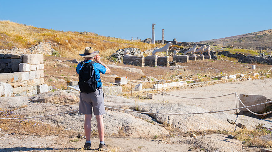 A man with a backpack views the Terrace of the Lions at the Delos Archaeological Site.