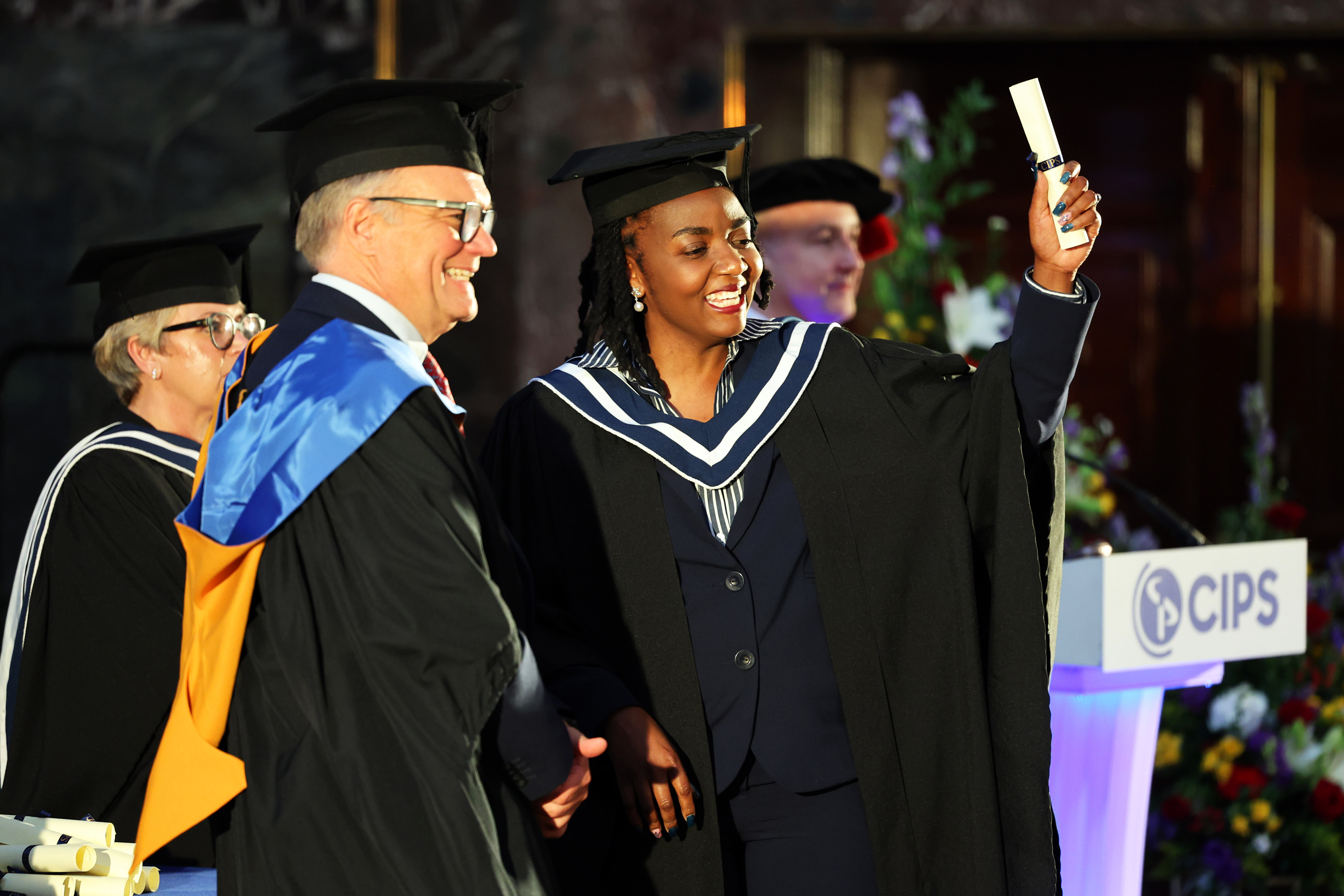 Female graduate in cap and gown on the stage receiving her diploma from CIPS CEO