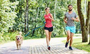 Športen par s psom teče na poti v parku.