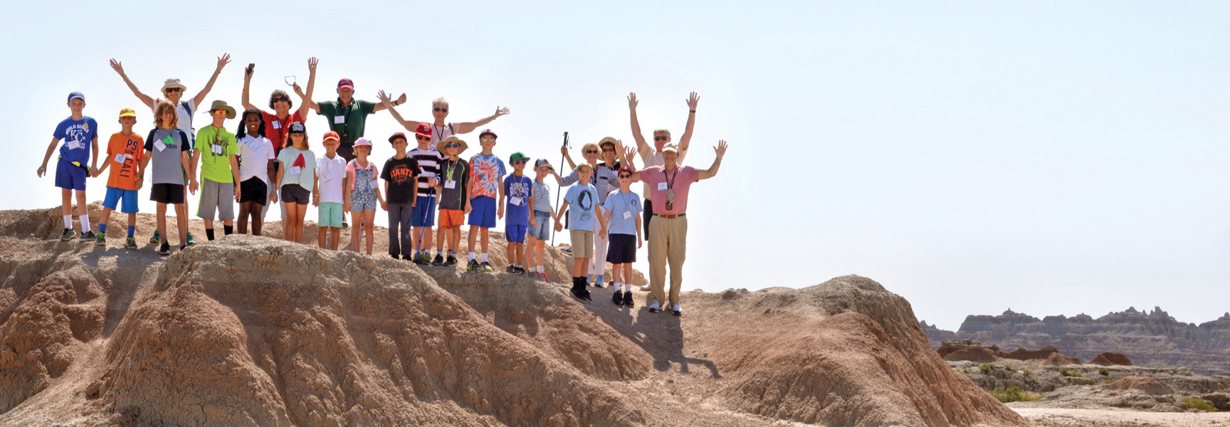 A large family group of adults and children wave from the top of a butte in the South Dakota Badlands.
