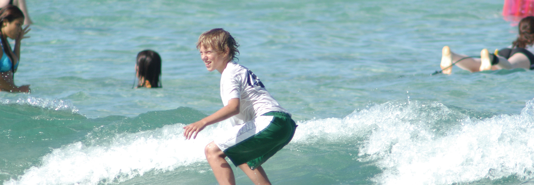 A young boy smiles as he learns to surf on a wave in the turquoise waters of Hawaii.