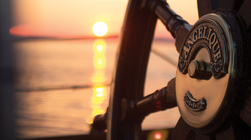 Close-up of the wooden steering wheel of the windjammer Angelique during a sunset over the Maine coast.