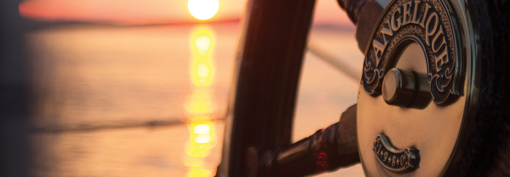 Close-up of the wooden steering wheel of the windjammer Angelique during a sunset over the Maine coast.
