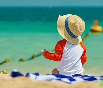 Otrok na plaži, starši upoštevajo navodila za izpostavljanje soncu oziroma sončenje.