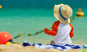Otrok na plaži, starši upoštevajo navodila za izpostavljanje soncu oziroma sončenje.