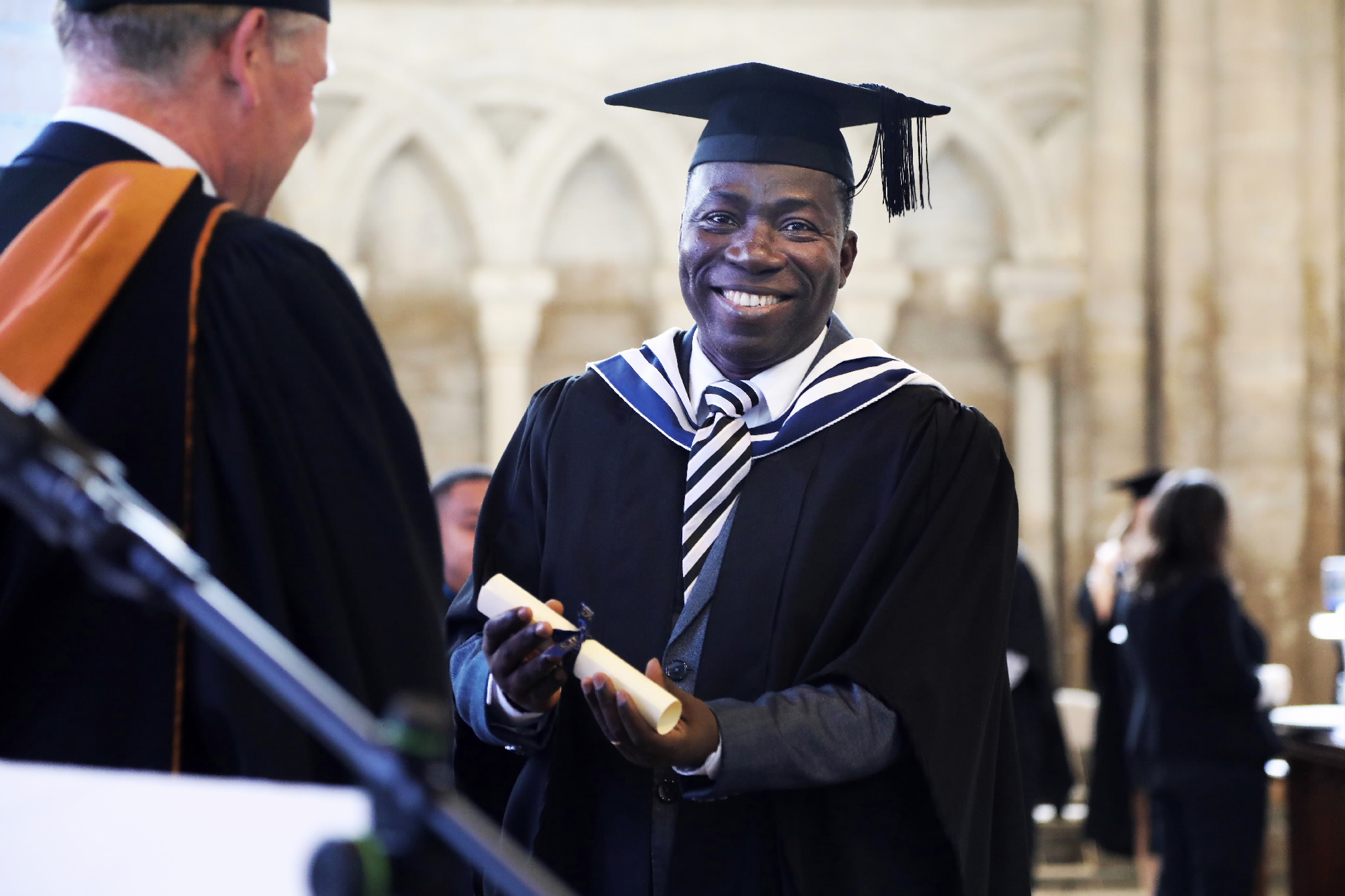 A smiling male graduate holds his rolled-up diploma